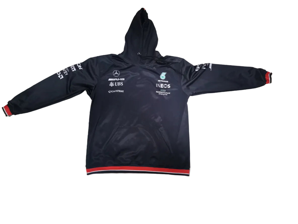 A black Mercedes Formula 1 team hoodie jacket with red and white stripes on the cuffs and hem, laid flat on a light gray tiled floor. The jacket features white sponsor logos and text, including Mercedes-Benz, F1, and Castore.
