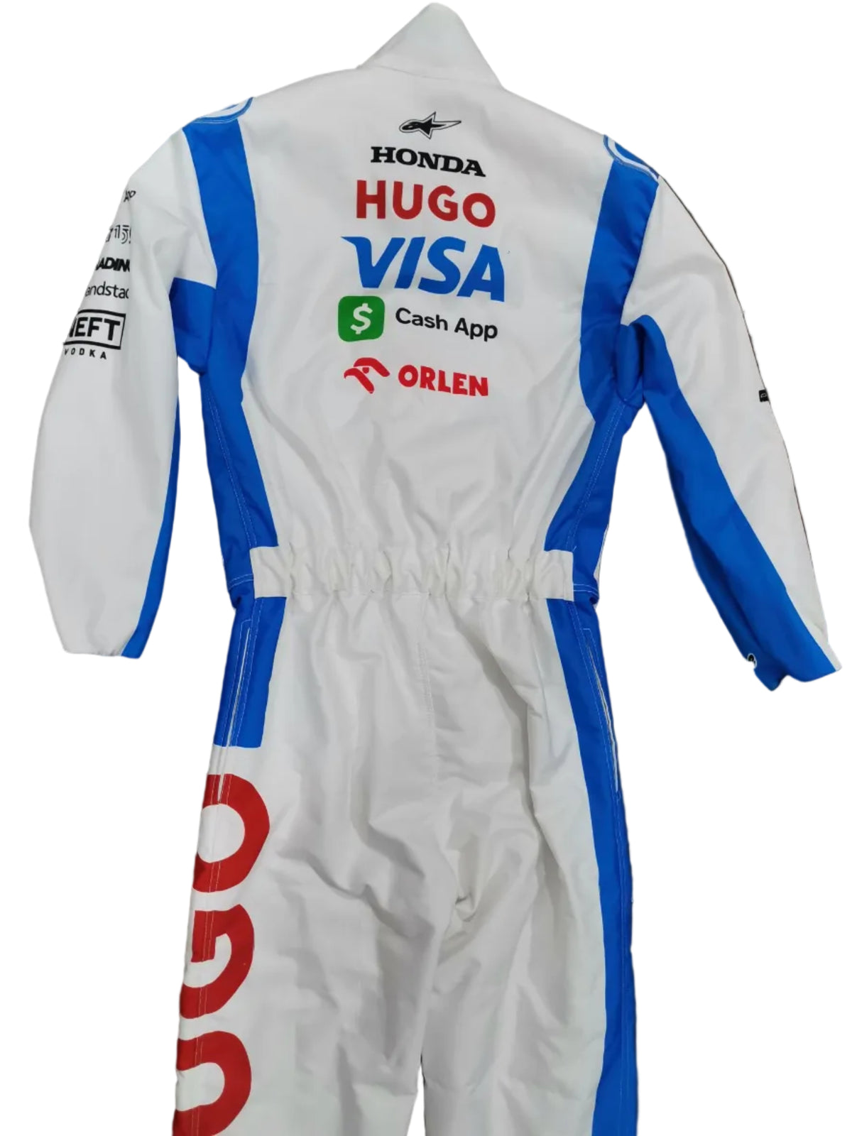 A white and blue racing suit laid flat on a brown floor, featuring sponsor logos including Honda, Hugo VISA, Cash App, and Orlen. A bare foot is visible at the bottom right corner.