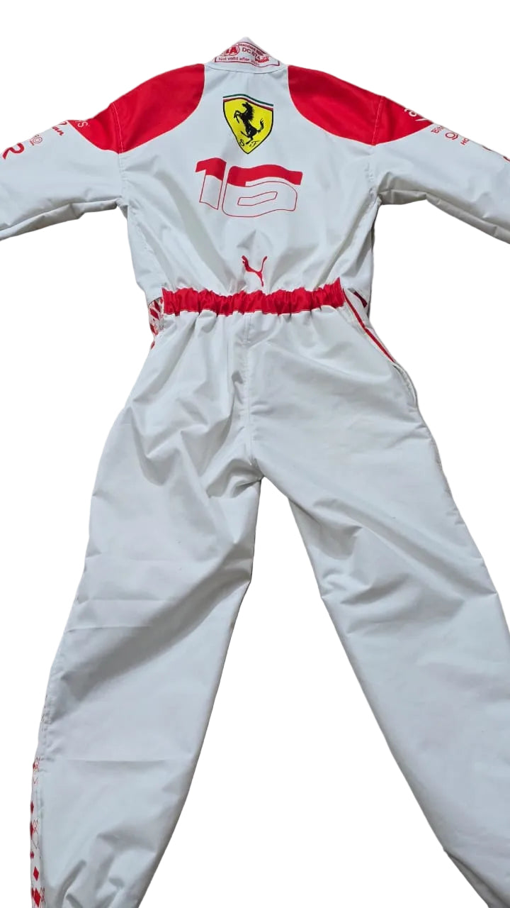 A white and red Puma Ferrari racing suit laid flat on a beige tiled floor. The suit features the yellow Ferrari shield logo on the chest, the number 16, and Puma branding.