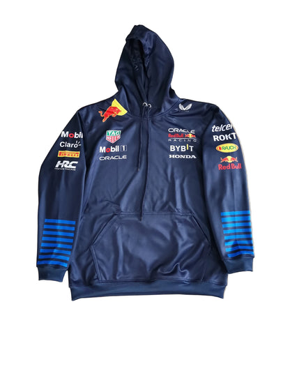 A navy blue Red Bull Racing zip-up hoodie with multiple sponsor logos, laid flat on a beige marble-patterned floor. The hoodie features the Red Bull logo on the chest, sponsor logos such as Mobil 1, Oracle, and Red Bull on the sleeves and chest, and blue striped accents on the cuffs.