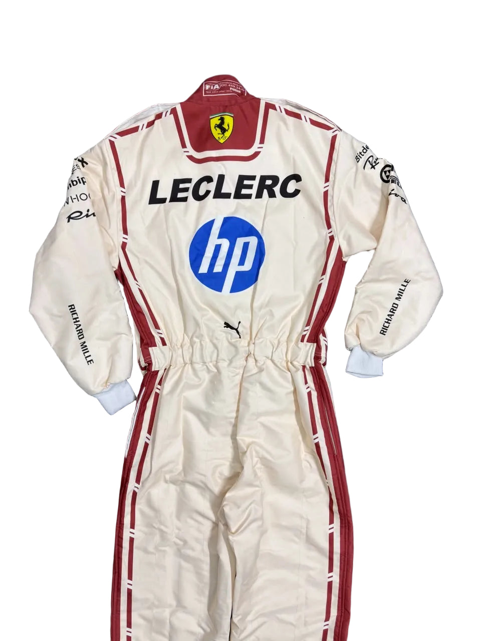 A cream and red Leclerc racing suit with prominent HP and Ferrari logos, laid flat on a dark blue sheet.