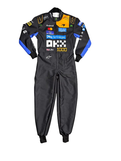 A black long-sleeve racing suit with blue and yellow sponsor logos, laid flat on a gray marble tile floor. Bare feet are visible at the bottom corners of the frame.