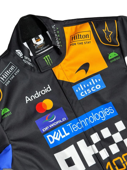 A close-up of a black racing team jacket featuring prominent sponsor logos including Hilton, Android, Mastercard, Cisco, Dell Technologies, and DP World, with a bright orange chest panel and a black collar.