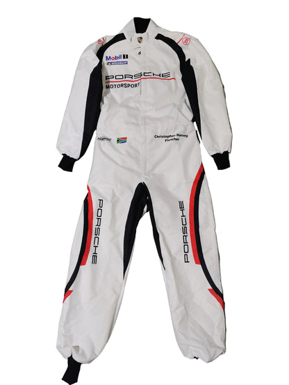 A white Porsche Motorsport racing suit with black and red side panels, laid flat on a gray marble-patterned tile floor. The suit features various sponsor logos including Mobil 1, Mobil 1 Racing, and Christian de Sousa Racing.